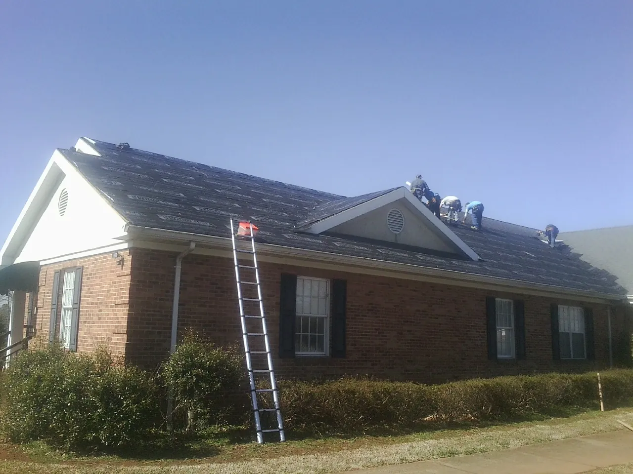 Crew tearing shingles off a brick ranch roof with a ladder set — Emergency Roof Repair work by our crew in Ophiem