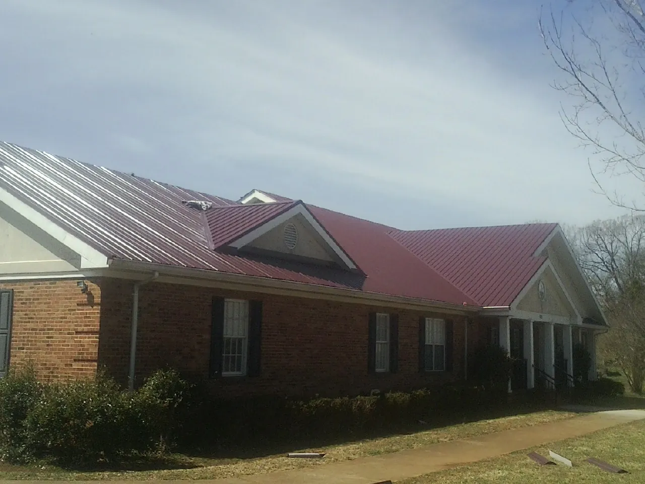 Red metal roof with gabled entries on a long brick building, from a Hail Damage Roof Repair job in Ophiem