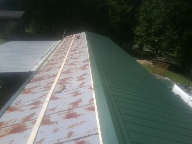 Old rusted panels beside newly installed green metal roofing — Wind Damage Roof Repair by Roofing Brothers in Ophiem