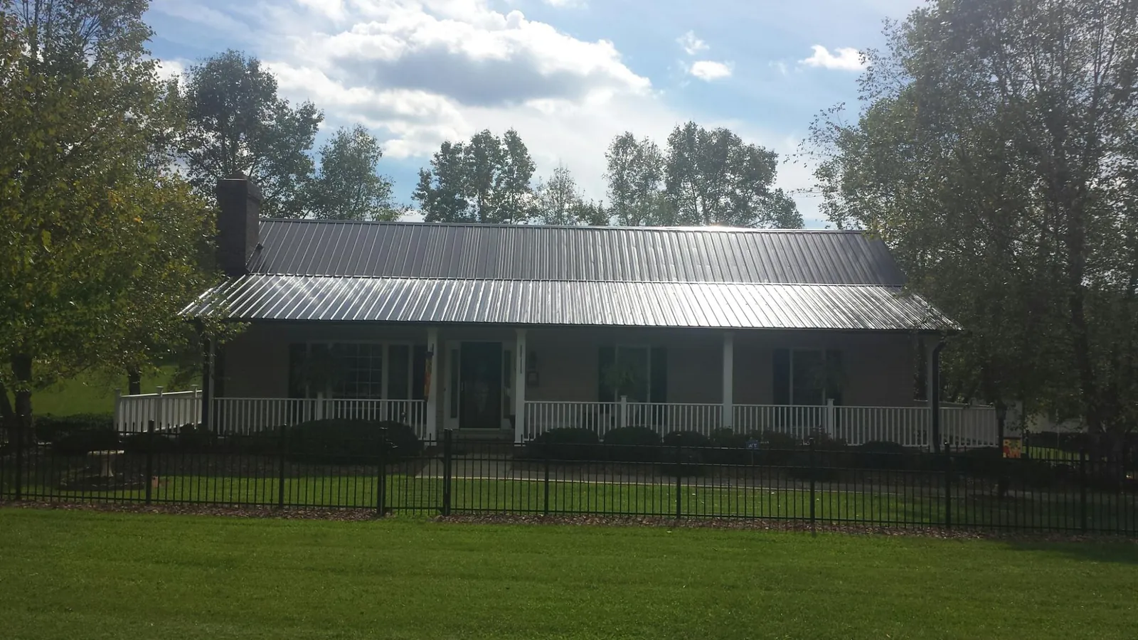 Gray metal roof on a brick ranch with a full width front porch — Gutter Guard Installation work by our crew in Ophiem