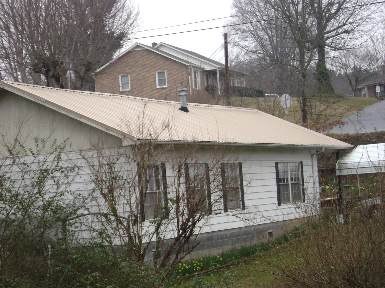 Tan metal roof on a white sided house set into a hillside — Commercial Roofing by Roofing Brothers in Ophiem
