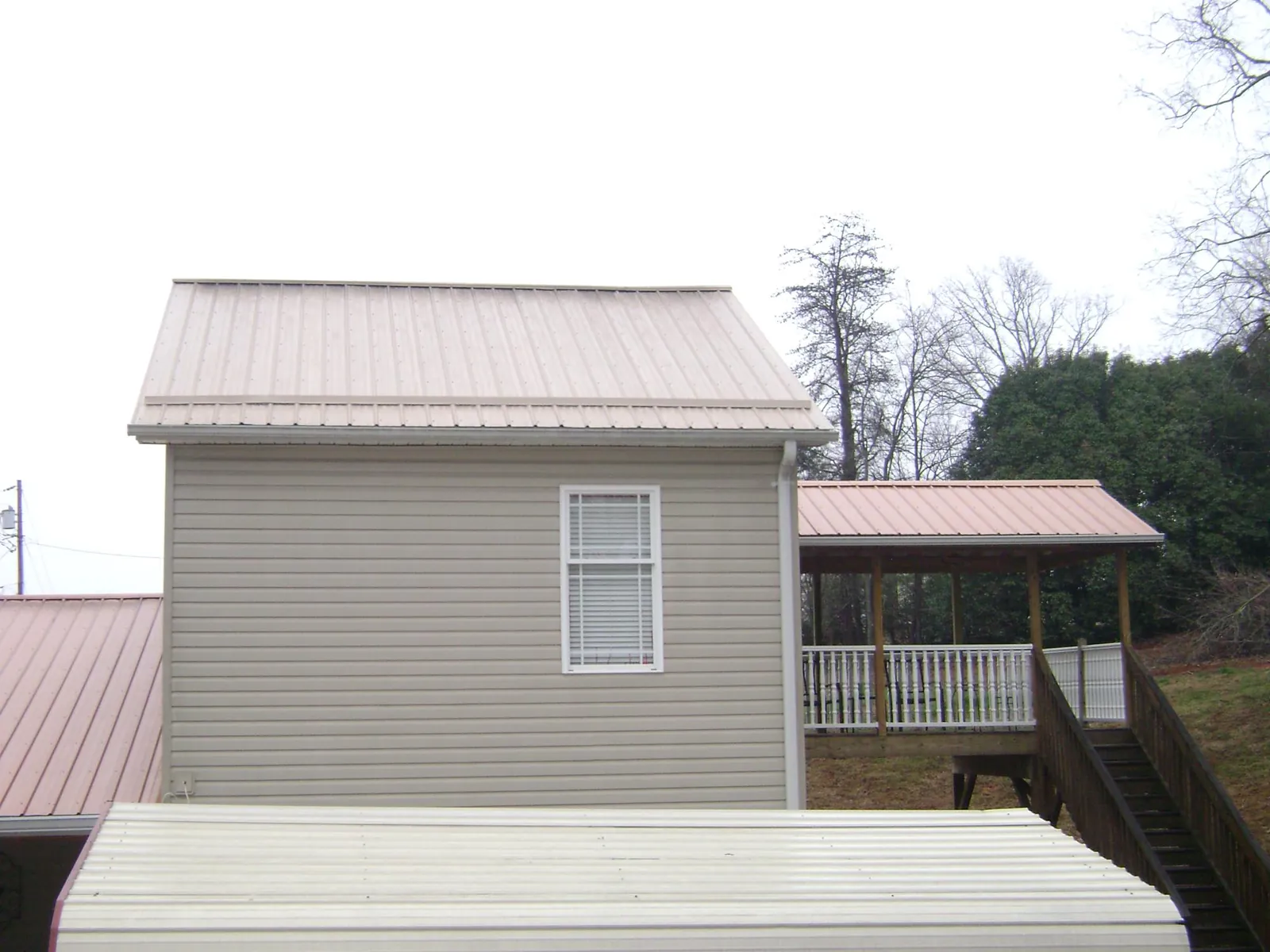 Tan metal roofs on a two story addition and attached porch, from a Roof Replacement job in Ophiem